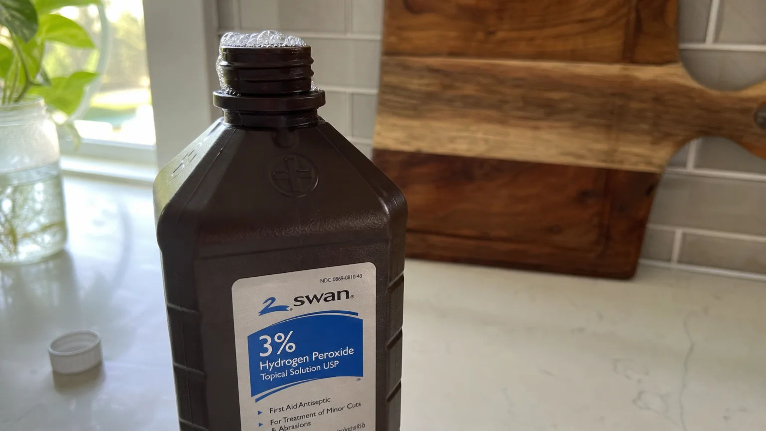 A brown bottle of hydrogen peroxide sits on a white kitchen counter with small bubbles fizzing at the opening.