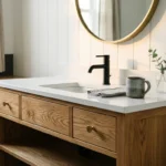 A modern white oak bathroom vanity with a black faucet, quartz countertop, and a brass mirror illuminated by morning light.