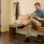 A warm, sunlit entryway featuring a person sitting on a newly built rustic pine farmhouse bench next to a potted plant.