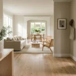 Bright foyer with light wood floors opening to a neutral living room with sofa, coffee table, and dining area.